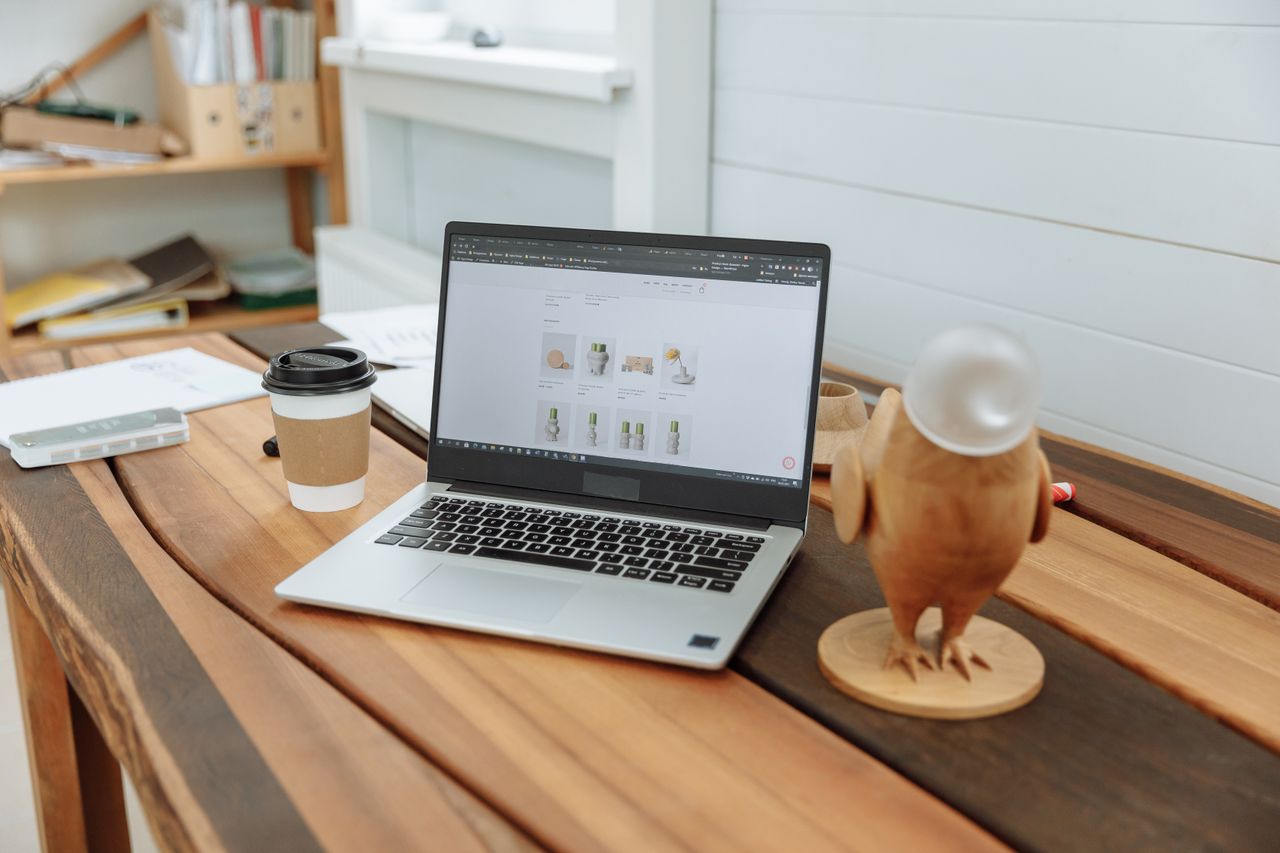 A modern office desk arrangement with a laptop, a coffee cup, and a wooden figurine placed on a wooden table.